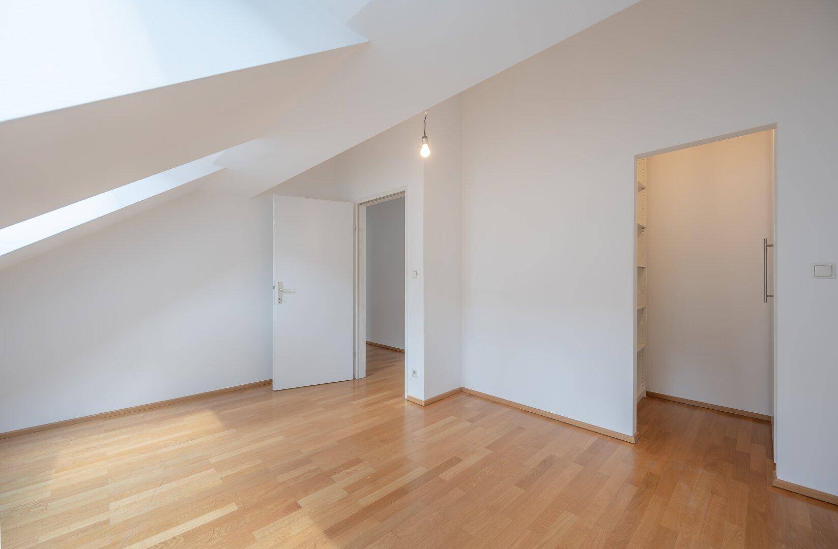 Schlafzimmer mit Holzboden, weiß gestrichenen Wänden und Zugang zu einem begehbaren Kleiderschrank.