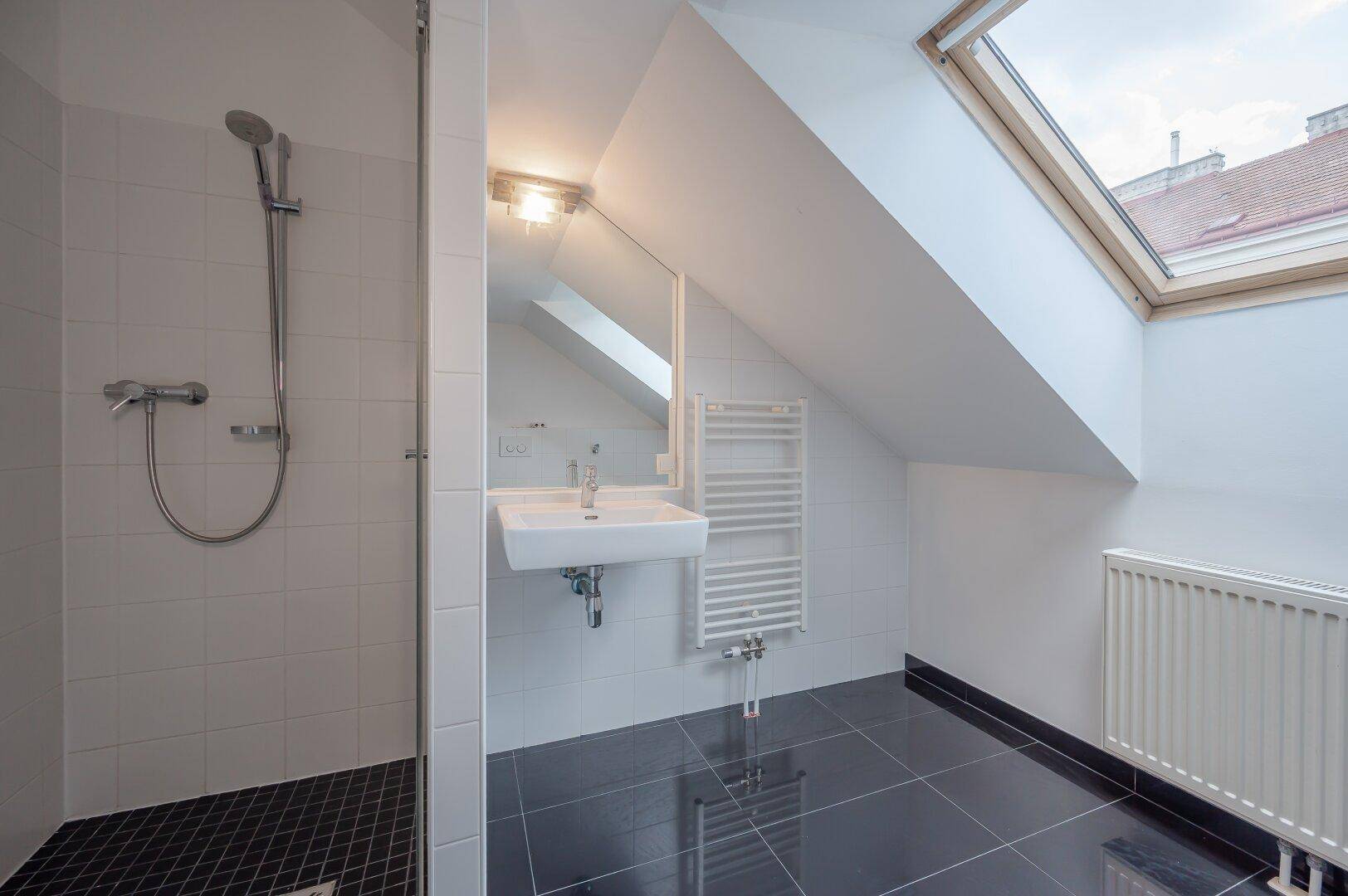 Helles Badezimmer mit Dusche, Waschbecken, beheiztem Handtuchhalter und Dachfenster.