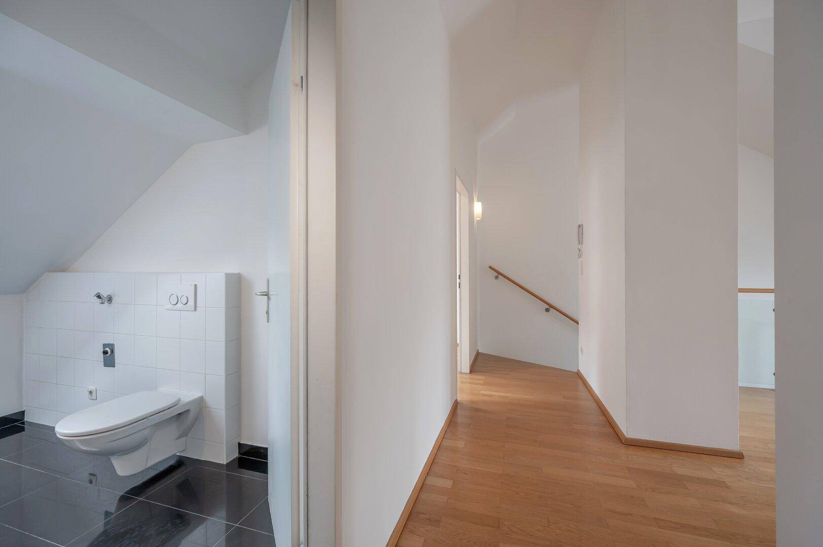 Flur mit Holzboden und Zugang zu einem Badezimmer mit Toilette.