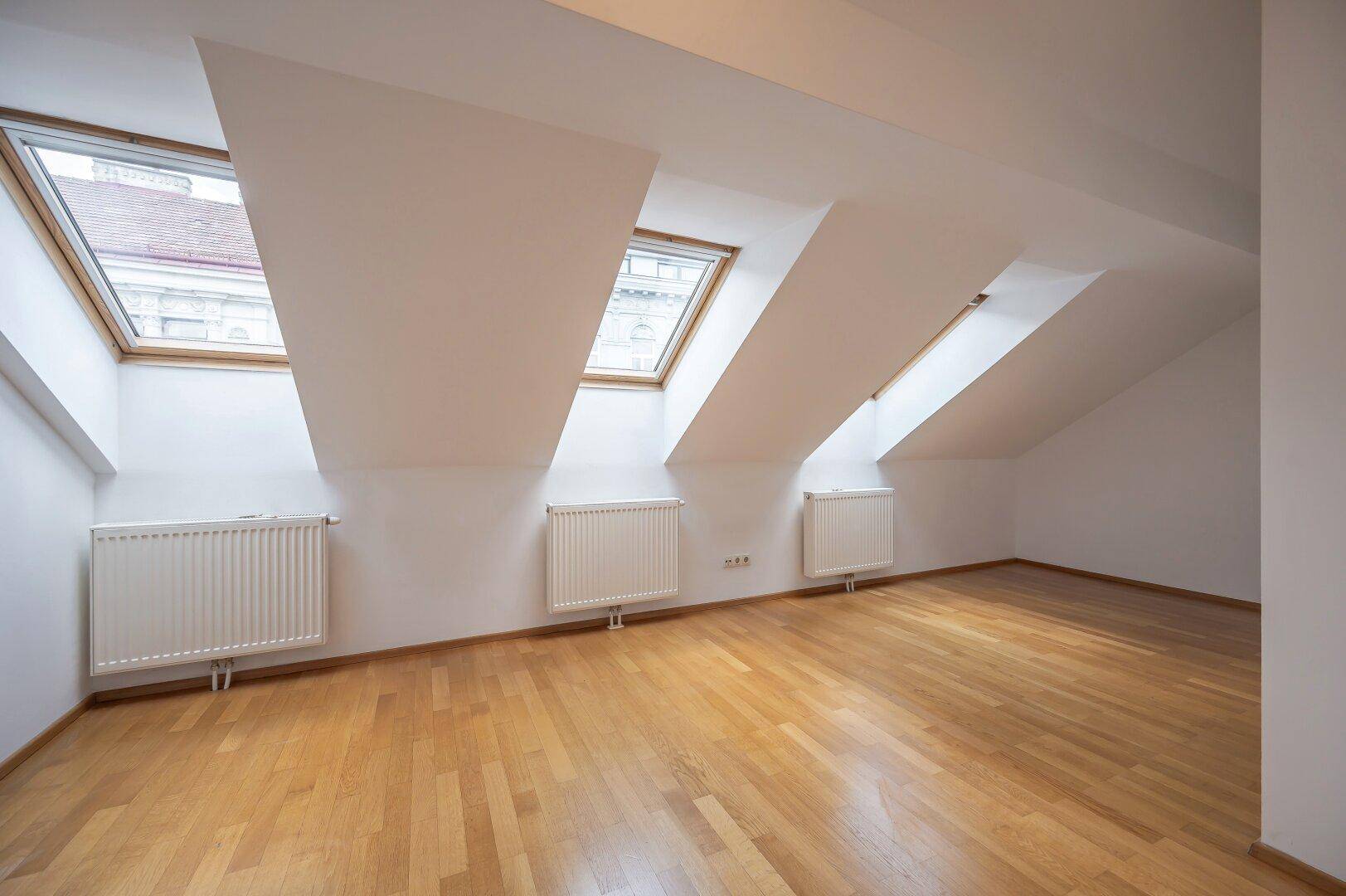 Geräumiges Zimmer mit Holzboden, Dachschrägen und mehreren Dachfenstern.