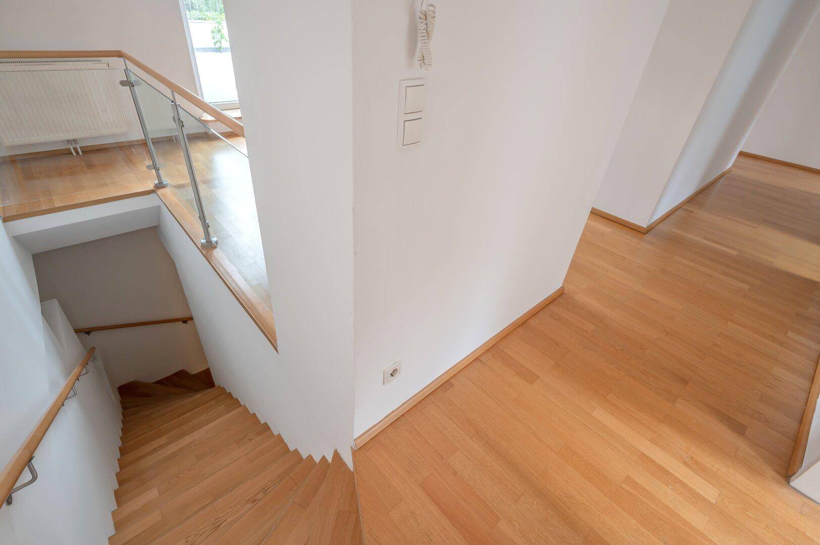 Treppenaufgang mit Holzstufen und Glasgeländer, der die Ebenen der Wohnung verbindet.
