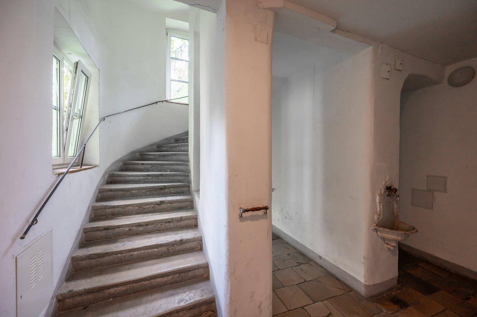 Historisches Treppenhaus mit Steinstufen und schmiedeeisernem Geländer.