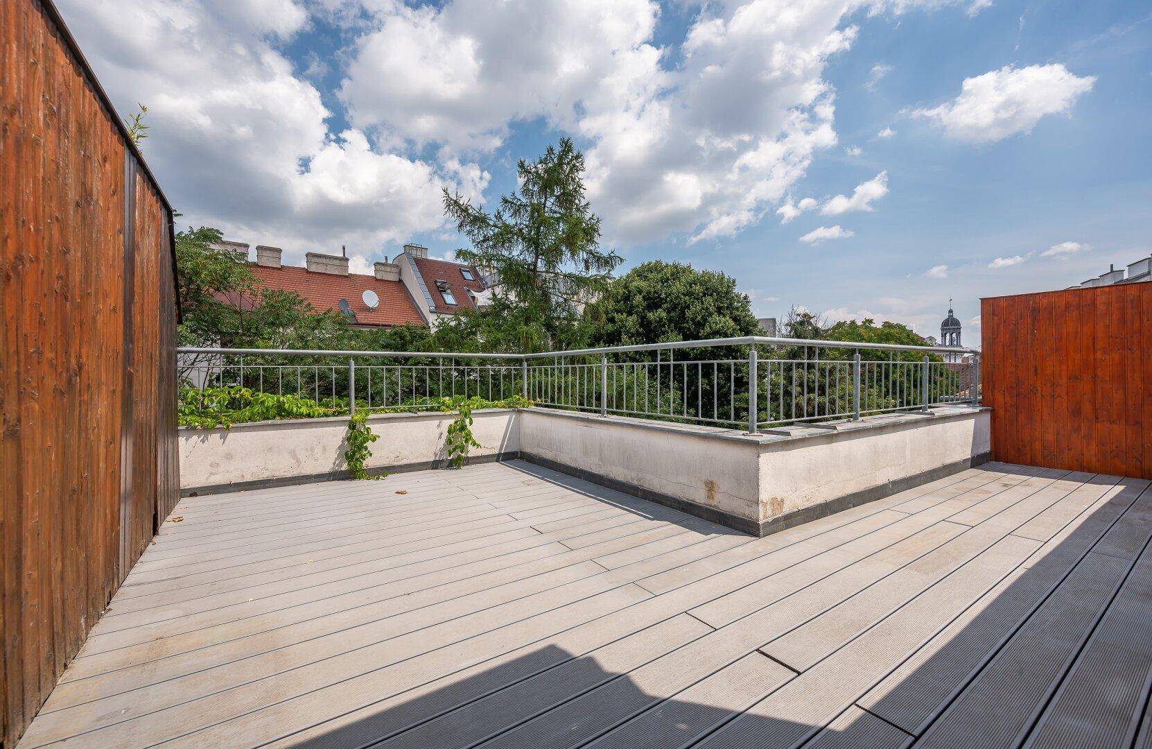 Weitläufige Dachterrasse mit Holzdielen und umgebender Begrünung.