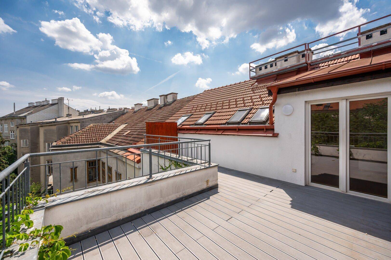 Große Dachterrasse mit Holzdielen und Blick über die Dächer der Stadt.