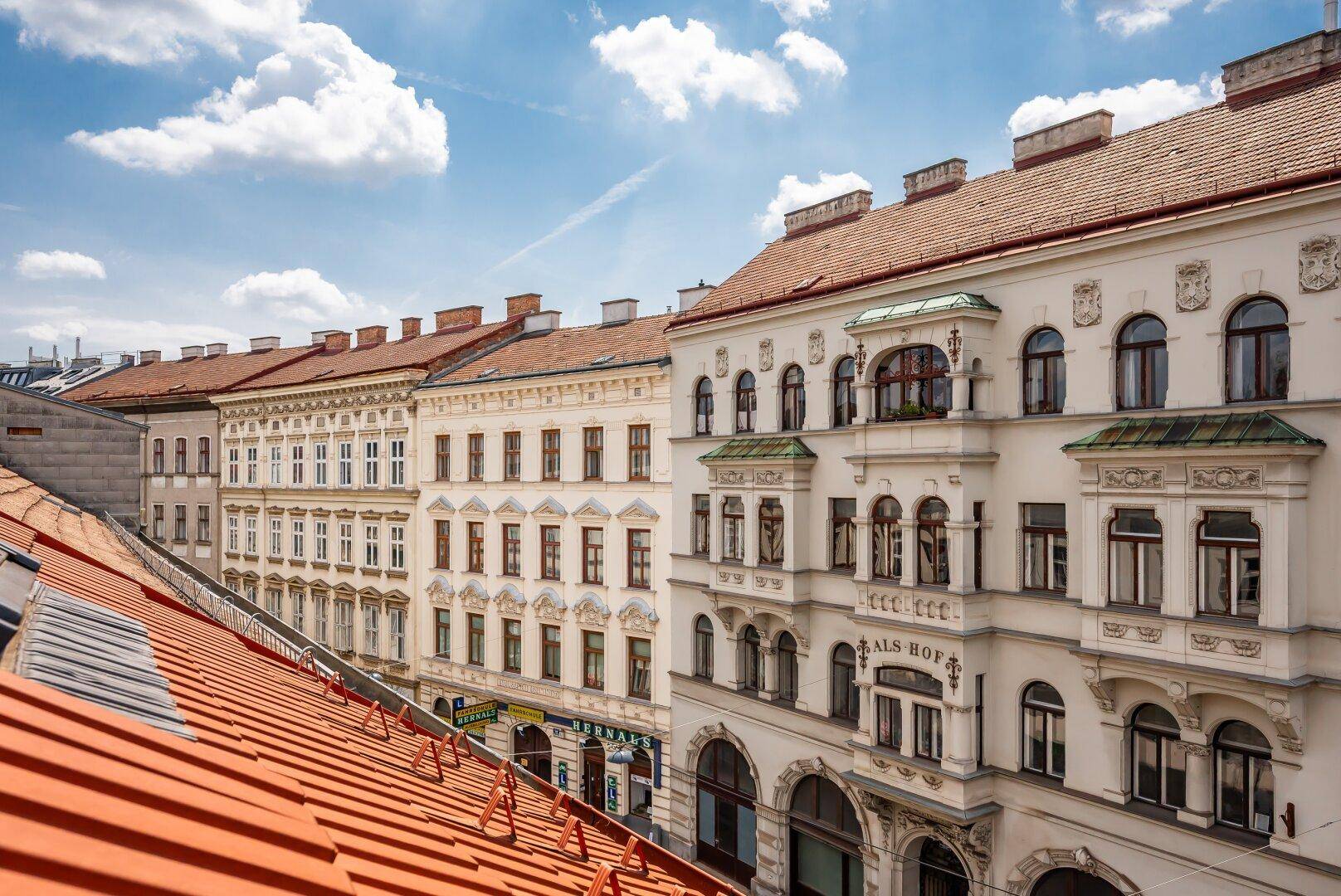 Dachansicht einer Straße mit historischen Gebäuden, weißen Fassaden und roten Ziegeldächern unter blauem Himmel.