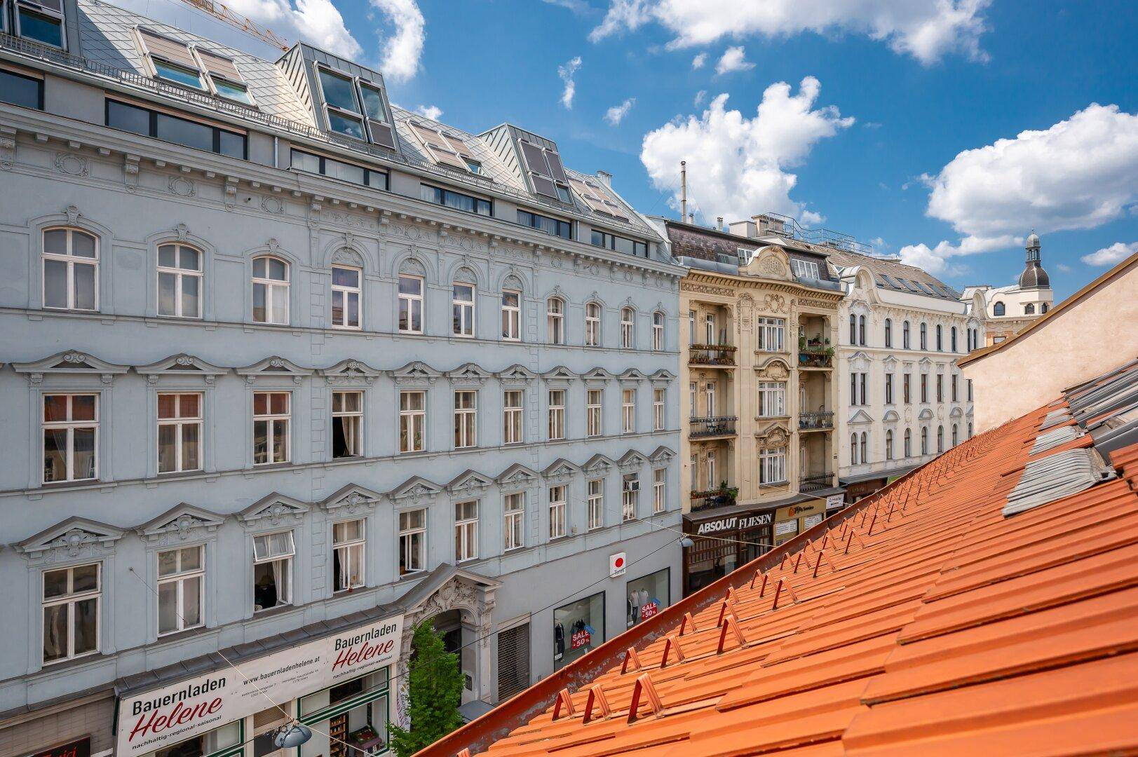 Panoramablick über Dächer und eine belebte Straße mit verschiedenen Gebäudefassaden und Geschäften.