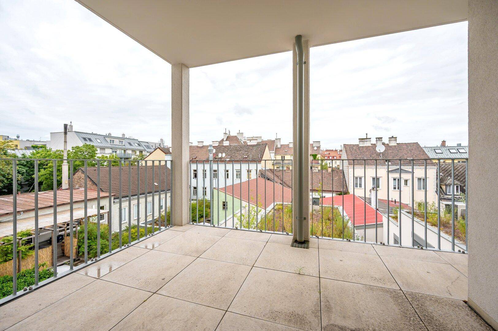 Großer Balkon mit Fliesenboden und Blick über die Dächer der Stadt.