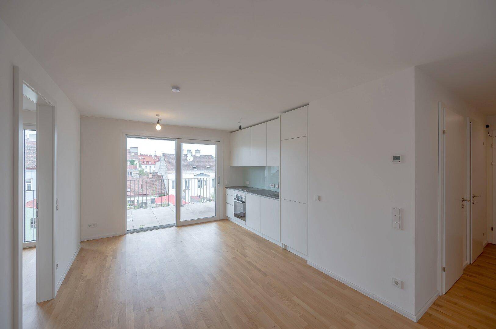 Heller Wohnbereich mit Holzboden und offener Küchenzeile, bietet Zugang zu einem Balkon.