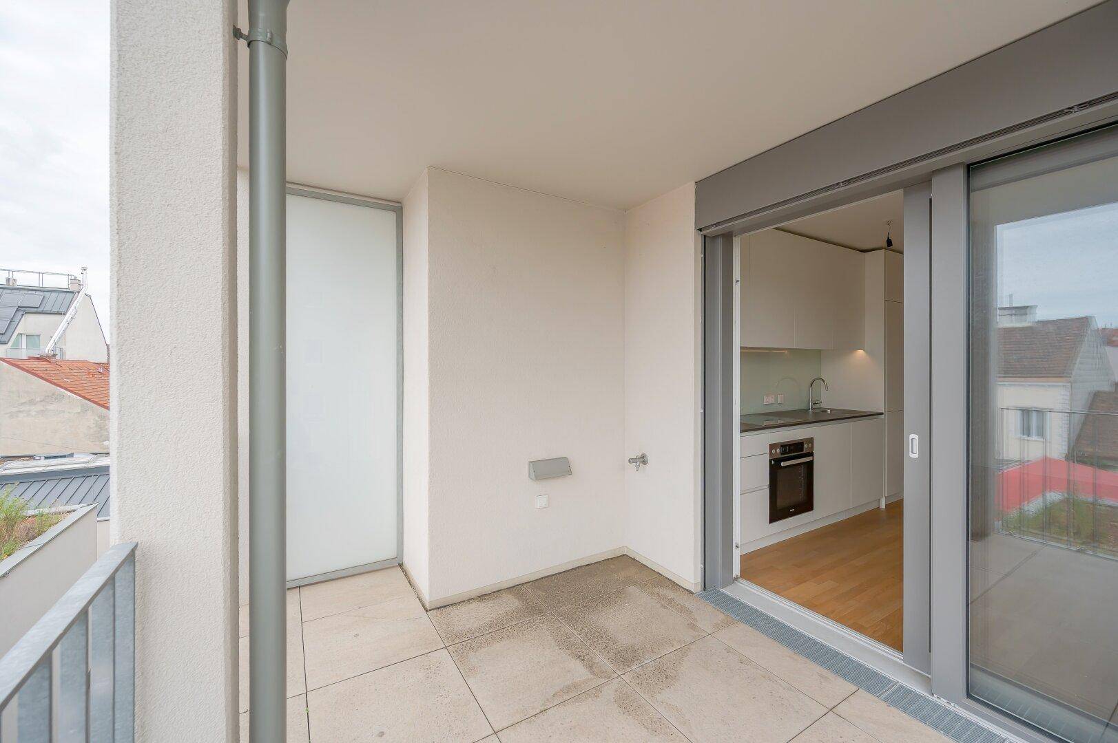 Balkon mit Fliesenboden und Blick in den Innenhof, direkt zugänglich von der Küche.