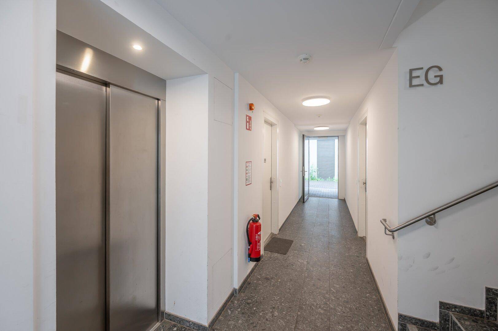Heller Flur im Erdgeschoss mit Aufzug und Treppenhauszugang.