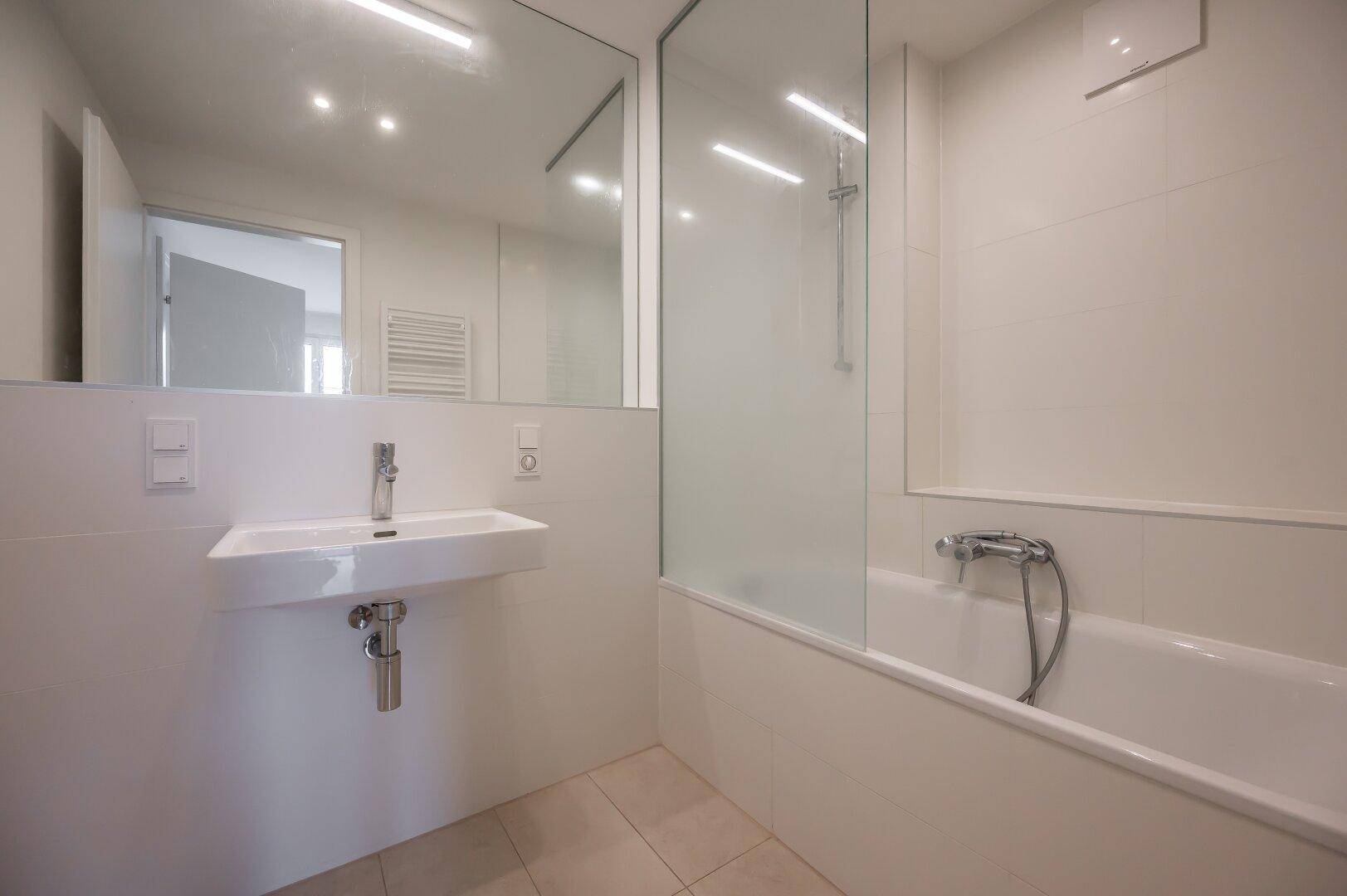 Modernes Badezimmer mit Badewanne, Dusche und großem Spiegel, hell gefliest.