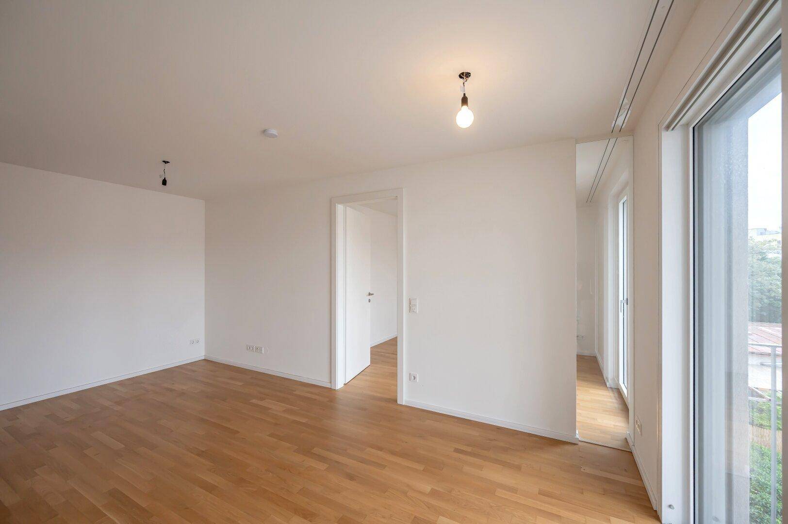 Geräumiger, heller Raum mit Holzboden und großen Fenstern, ideal als Wohn- oder Schlafzimmer.