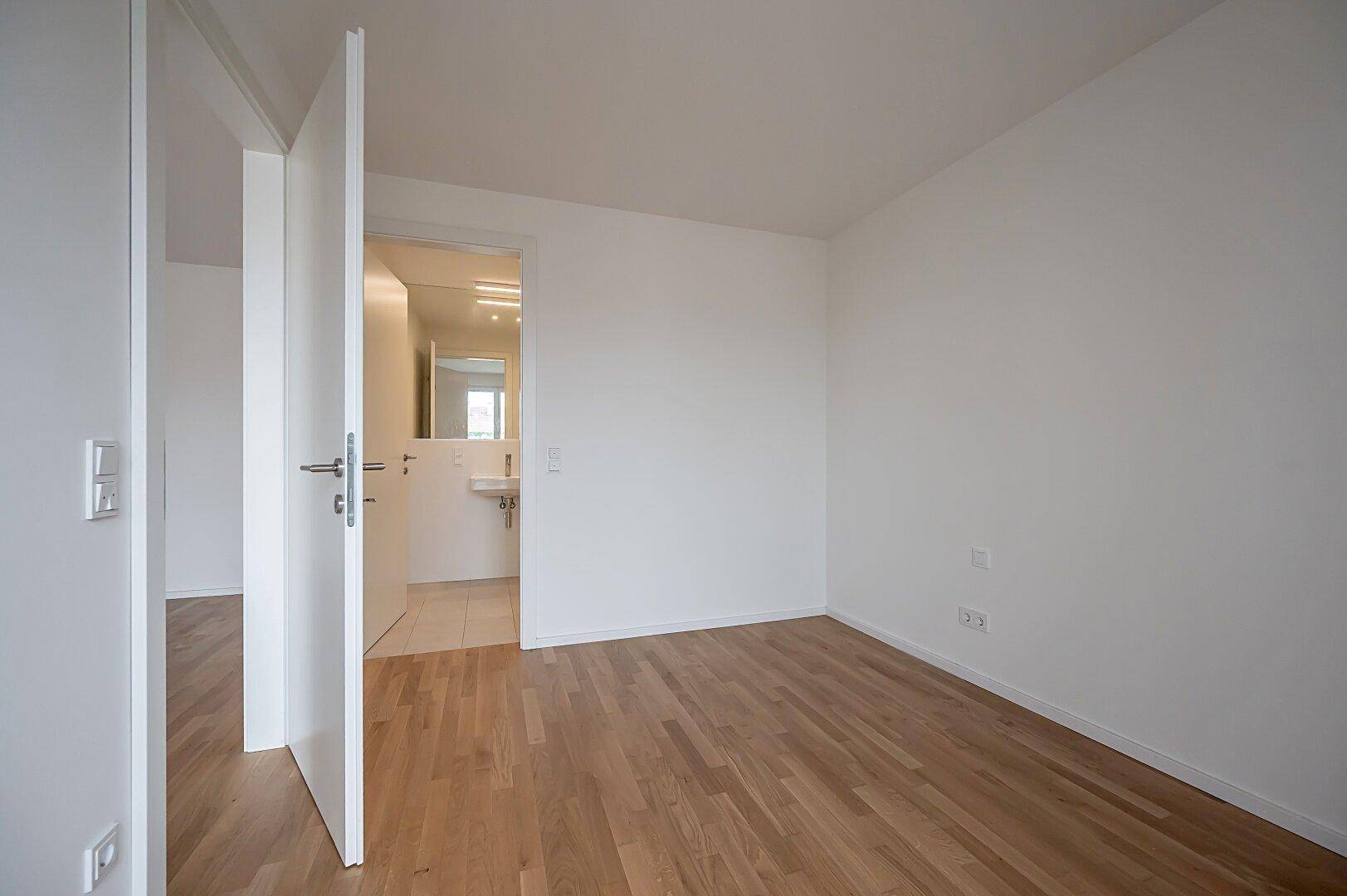 Helles Schlafzimmer mit Holzboden und Zugang zu einem angrenzenden Badezimmer.