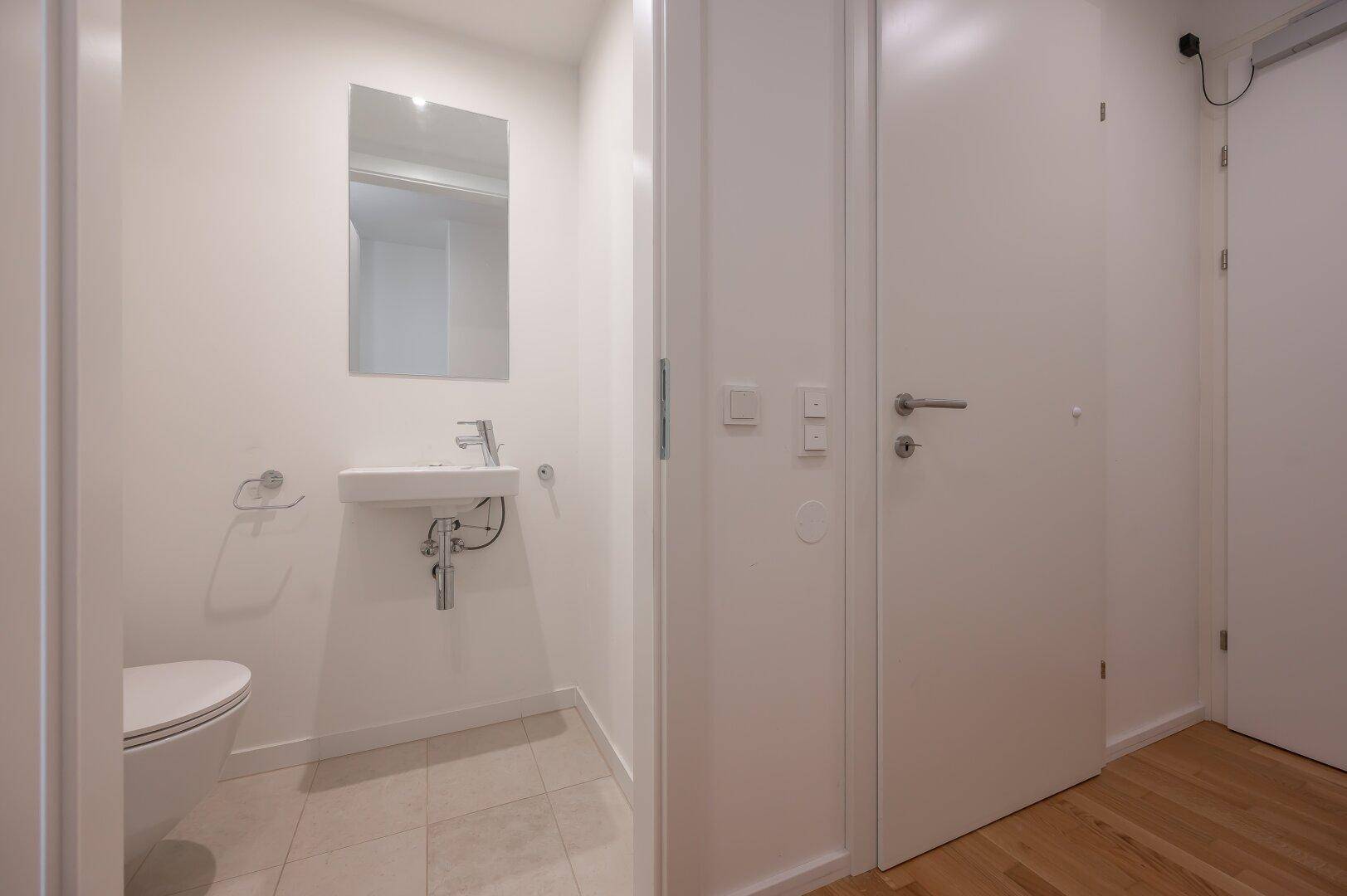 Modernes Gäste-WC mit Wand-WC, kleinem Waschbecken und Spiegel.