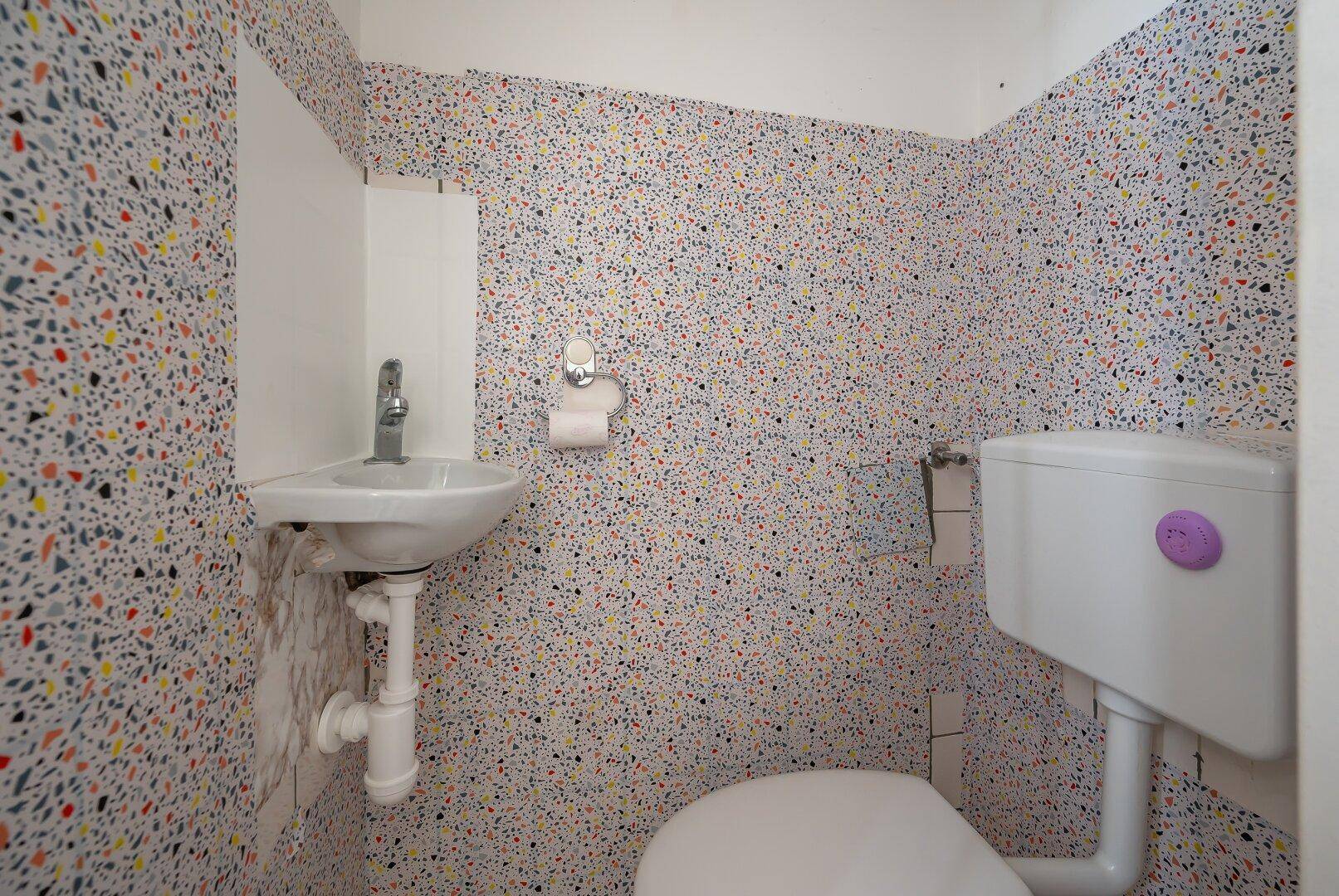 Kleine Gästetoilette mit farbenfroher Terrazzo-Optik an den Wänden und einem Eckwaschbecken.