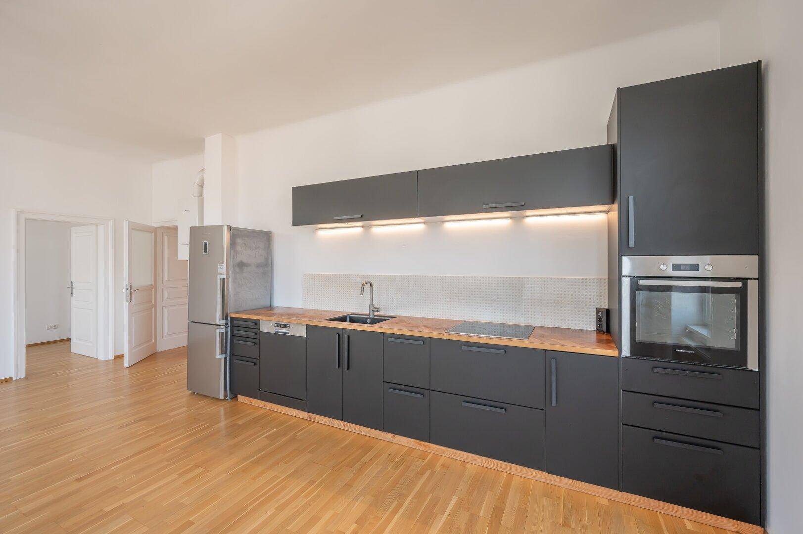 Moderne Einbauküche in Dunkelgrau mit Holz-Arbeitsplatte und integrierten Elektrogeräten.