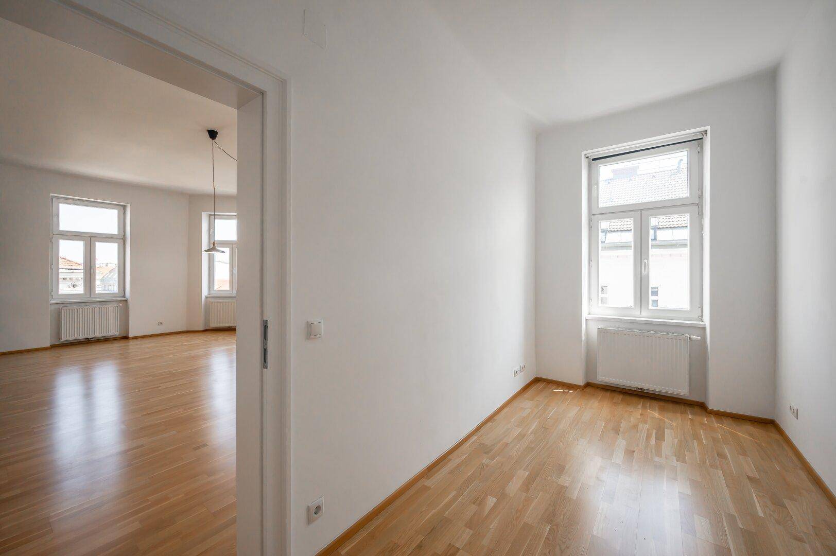 Blick durch eine Tür in den hellen Wohnbereich mit Parkettboden und weißen Wänden.