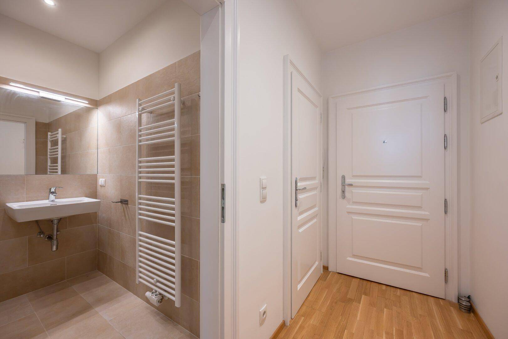 Modernes Badezimmer mit beigefarbenen Fliesen, Waschbecken und beheiztem Handtuchhalter.