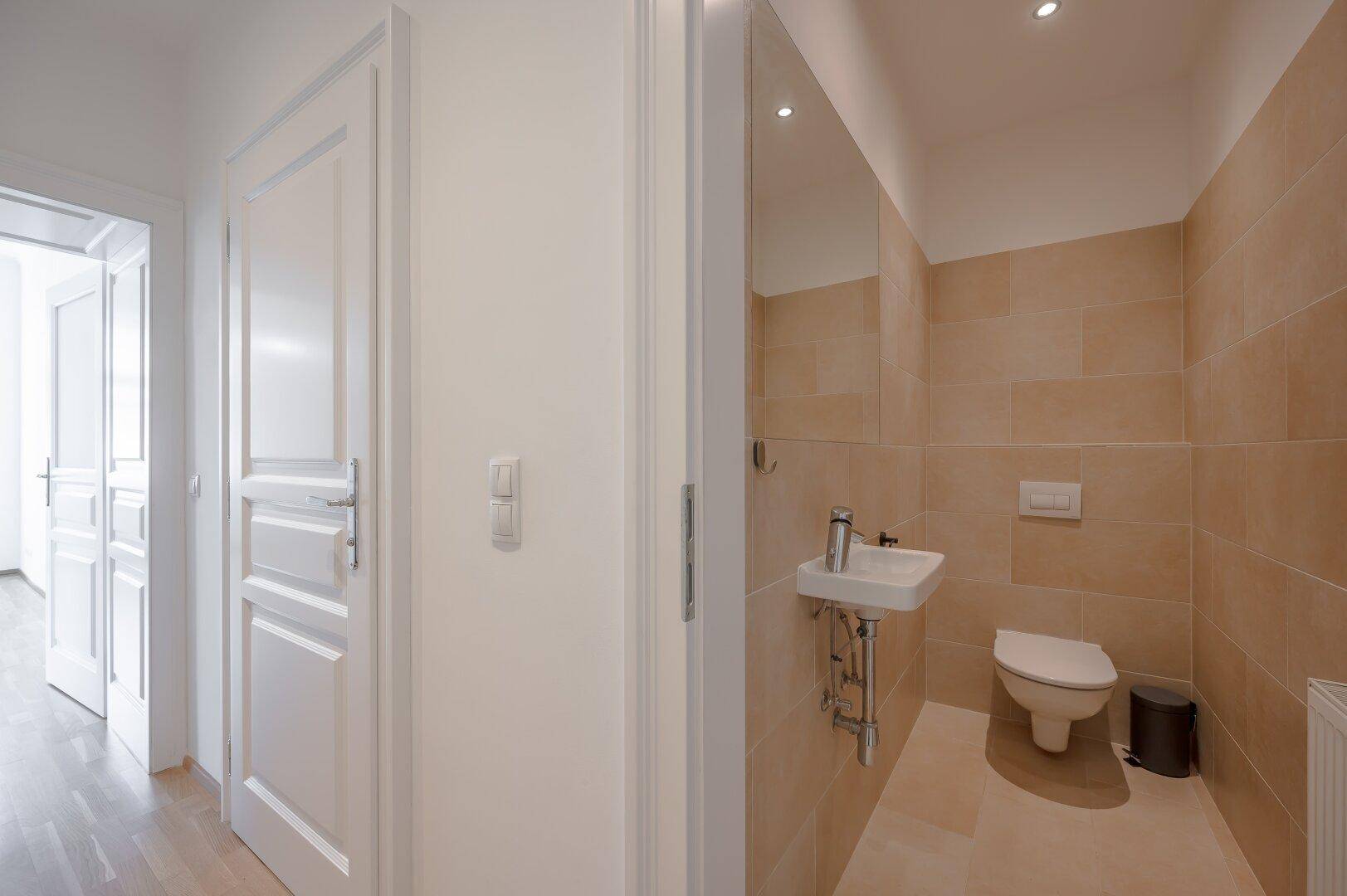Separates Gäste-WC mit beigefarbenen Fliesen, kleinem Waschbecken und Wand-WC.