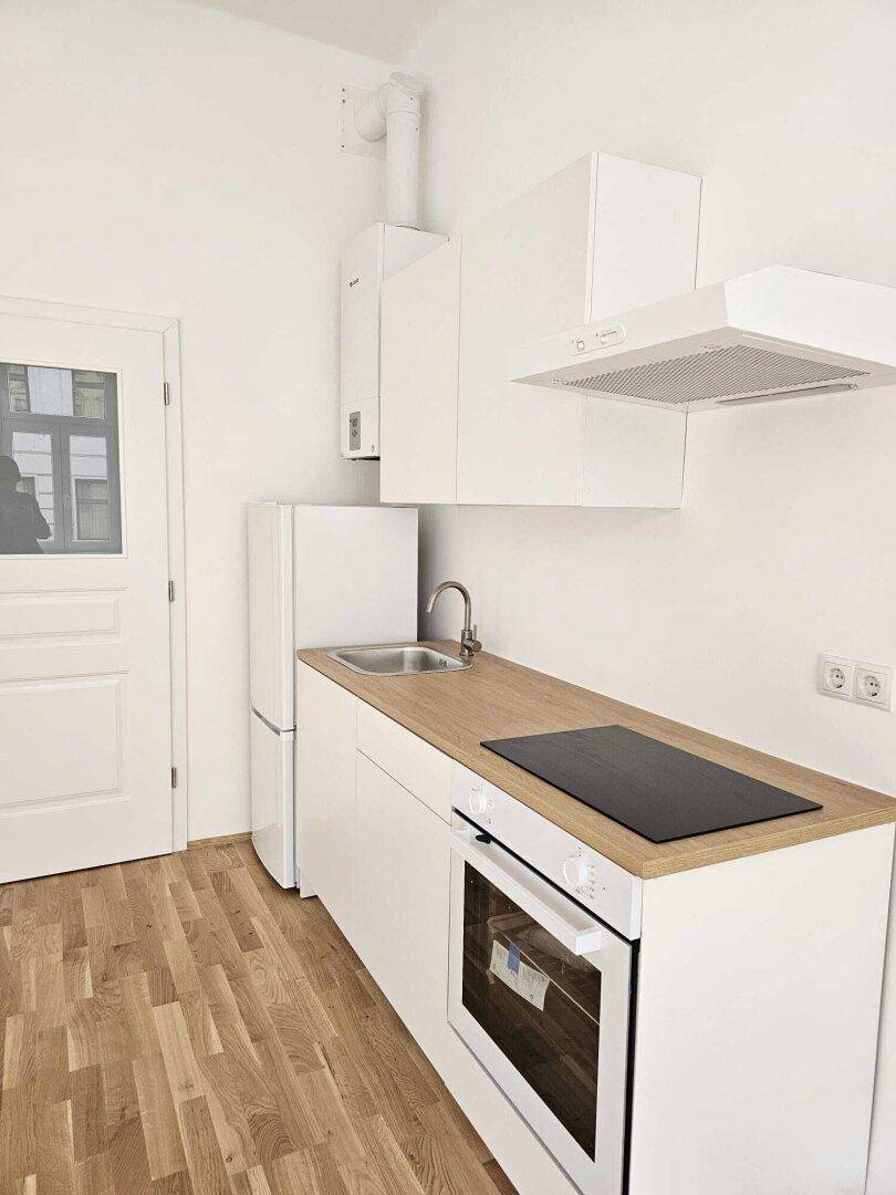 Moderne, helle Einbauküche mit weißen Schränken, Holz-Arbeitsplatte und Parkettboden.