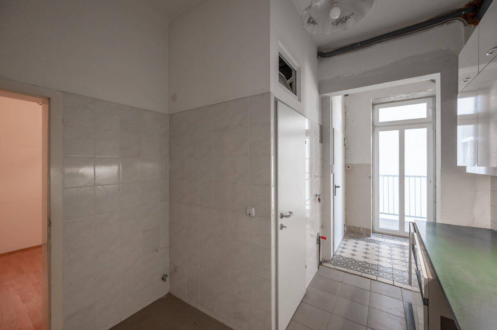 Küchenbereich mit gefliesten Wänden und Boden, führt zu einem kleinen Balkon.