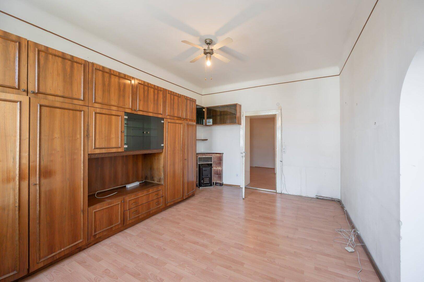 Helles Zimmer mit umfangreichen Holz-Einbauschränken und Deckenventilator.
