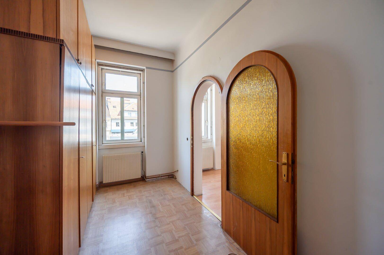 Flur mit Holz-Einbauschränken, Laminatboden und dekorativer Bogentür.