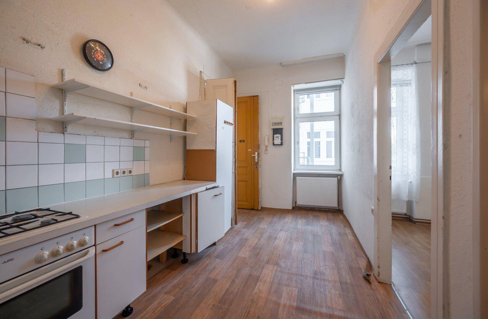 Küche mit Laminatboden, weißen Unterschränken, Herd und einem Fenster.
