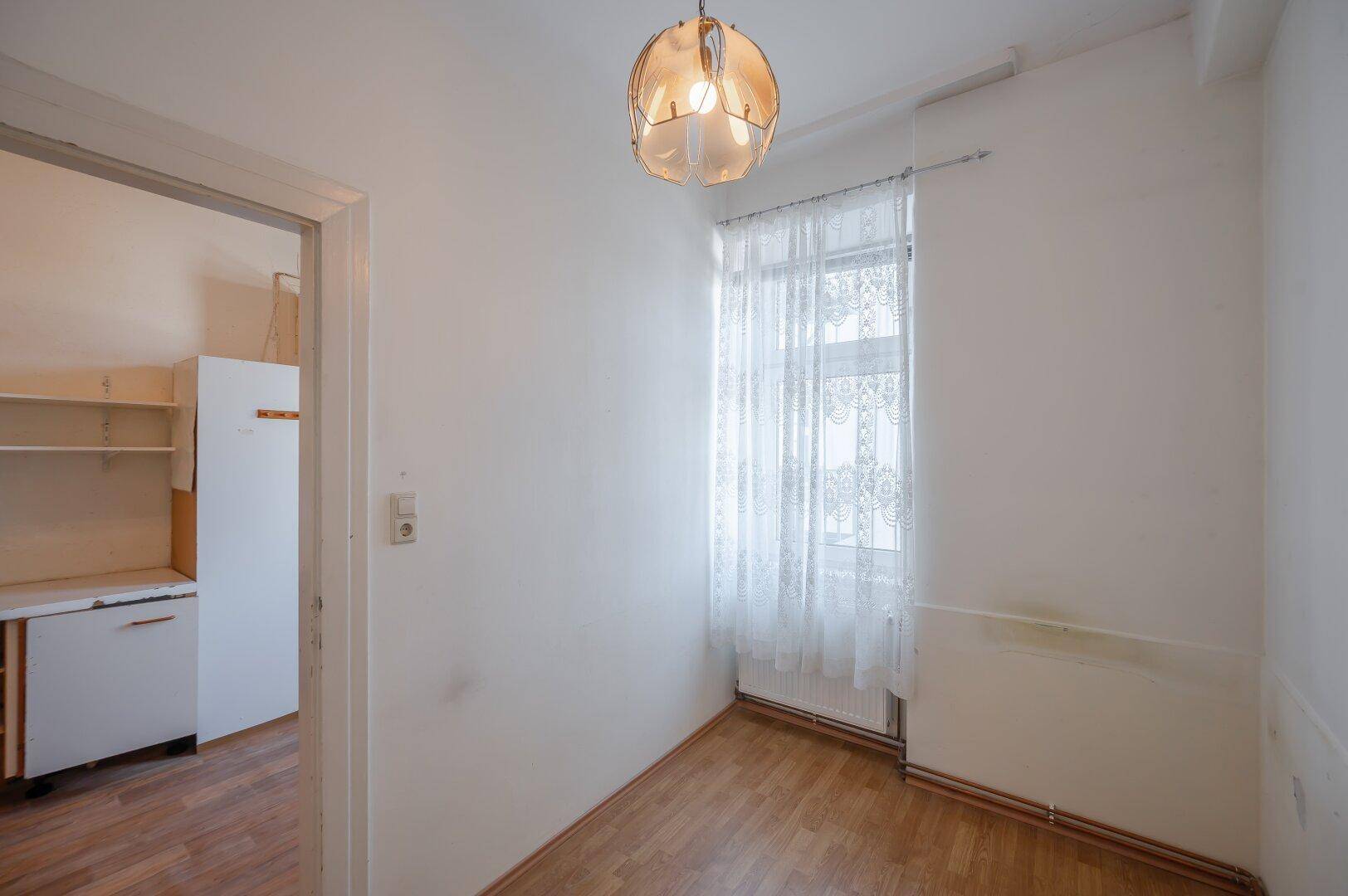 Kleiner Raum mit Laminatboden und Fenster, mit Blick in die Küche.