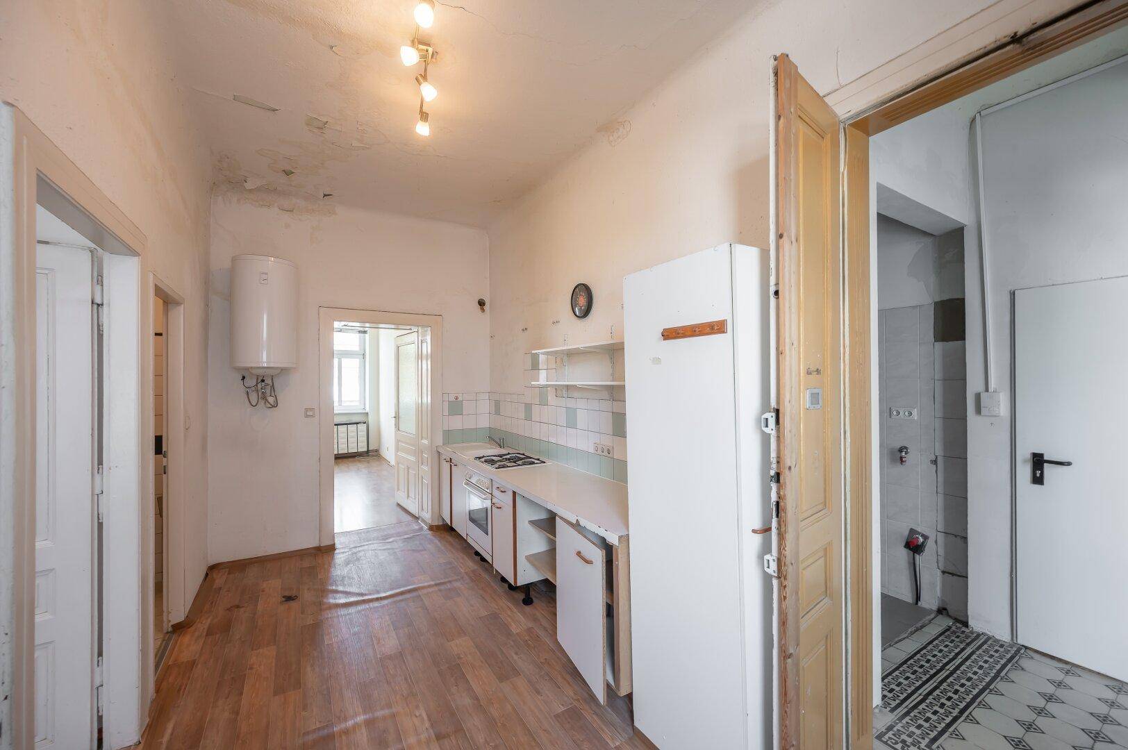 Küche mit Laminatboden, weißen Schränken, Herd, Kühlschrank und Warmwasserbereiter.
