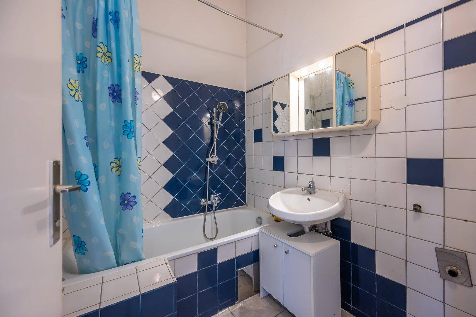 Badezimmer mit blauen und weißen Fliesen, Badewanne mit Dusche und Waschbecken.
