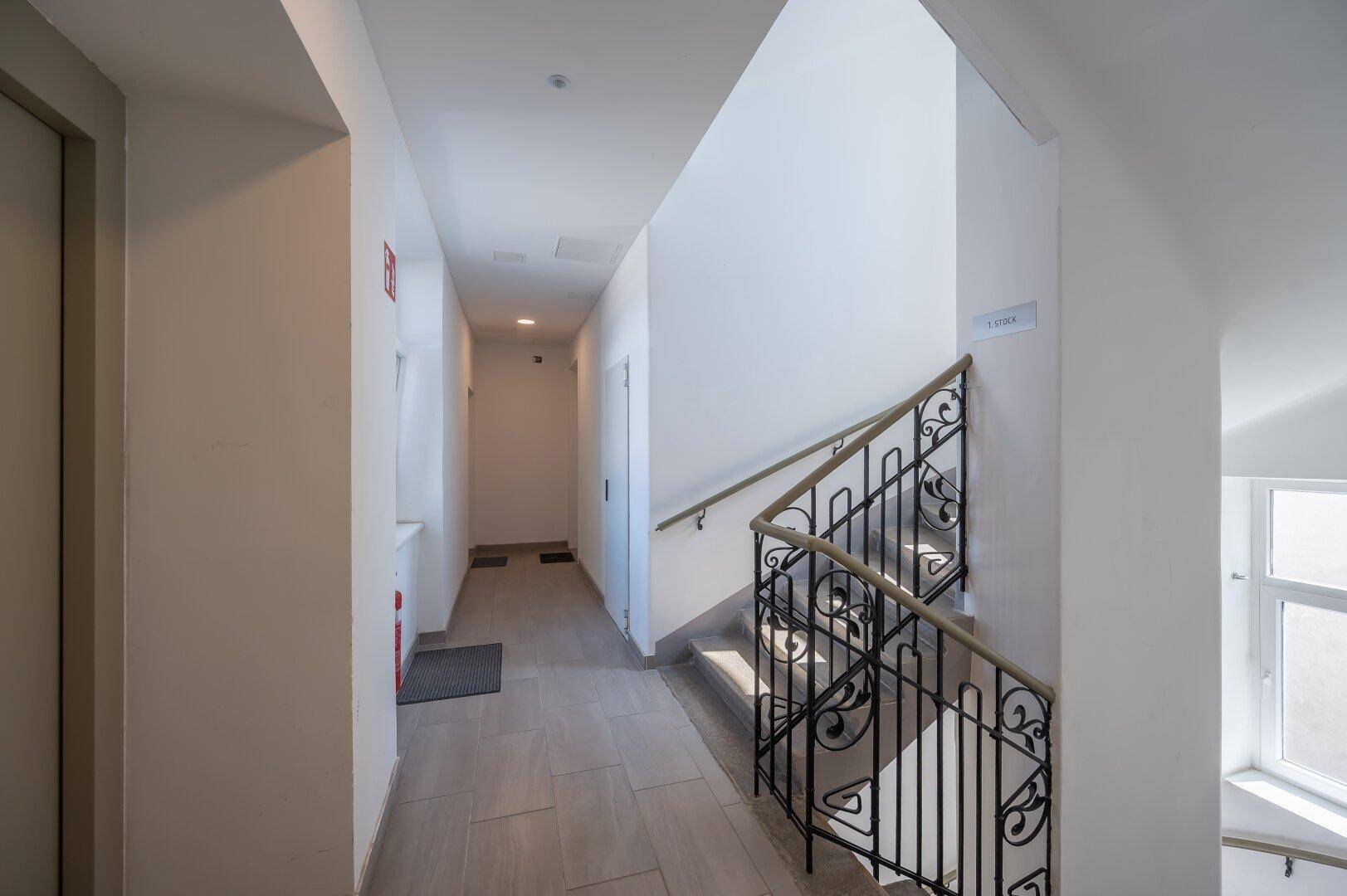 Heller Gemeinschaftsflur mit Treppe, Aufzug und Fliesenboden.