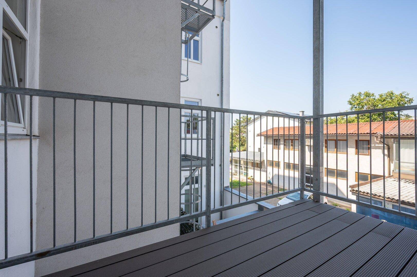 Balkon mit grauem Bodenbelag und Metallgeländer, bietet Blick auf umliegende Gebäude.