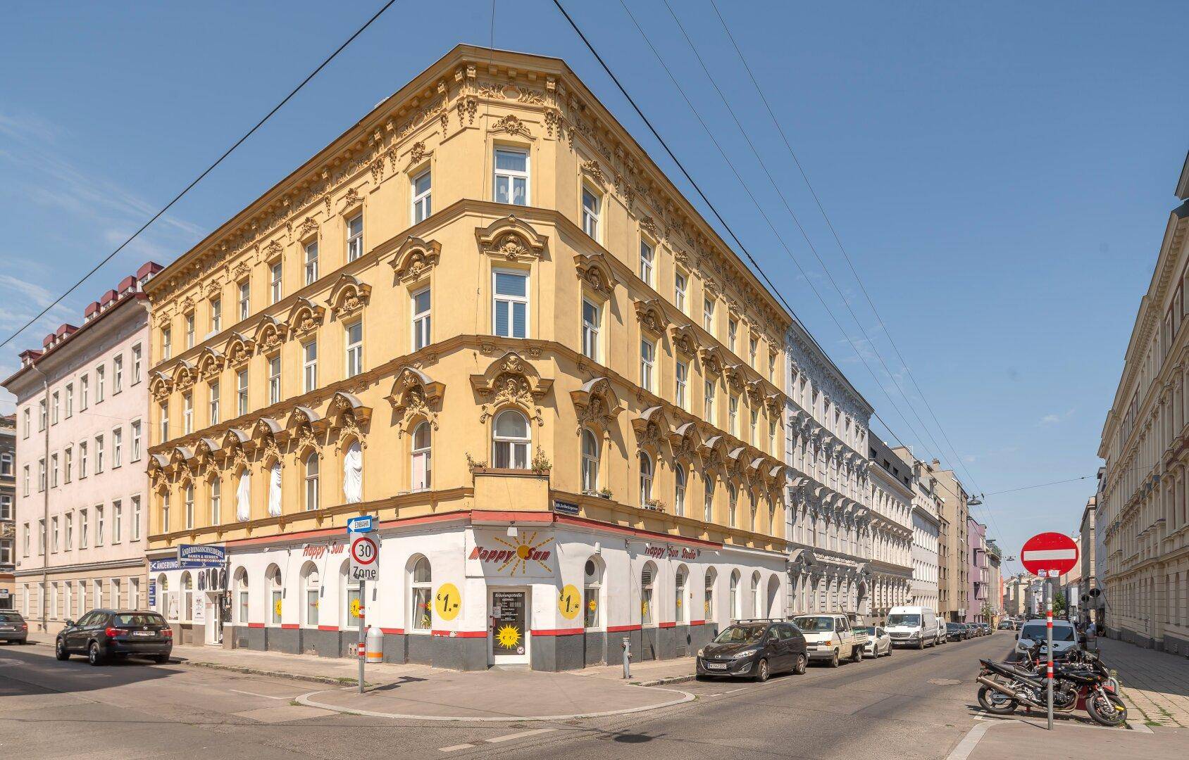 Historisches Eckgebäude mit gelber Fassade und vielen Fenstern an einer belebten Kreuzung.