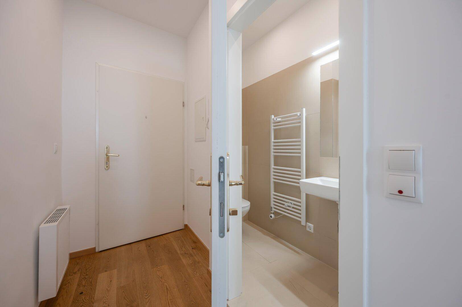 Heller Flur mit Holzboden und Zugang zu einem modernen Badezimmer mit Handtuchheizkörper.