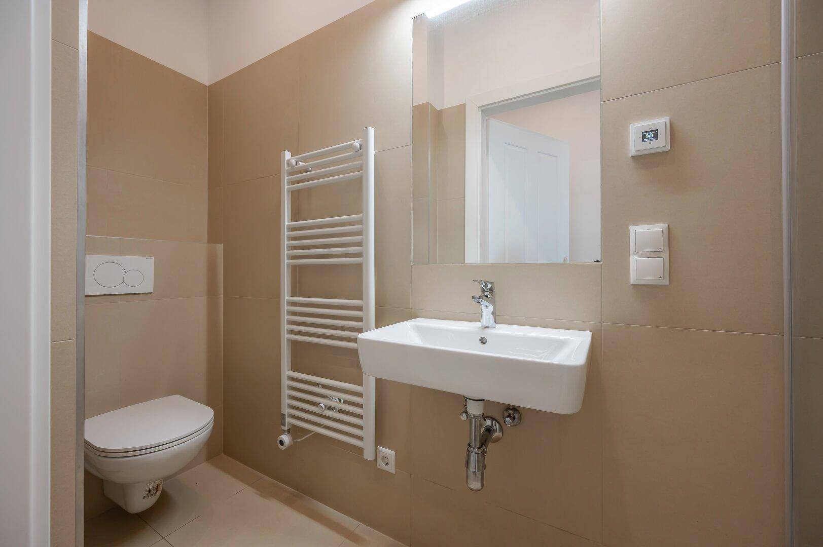 Modernes Gäste-WC mit Wand-WC, Waschbecken und beheiztem Handtuchhalter in neutralen Farbtönen.