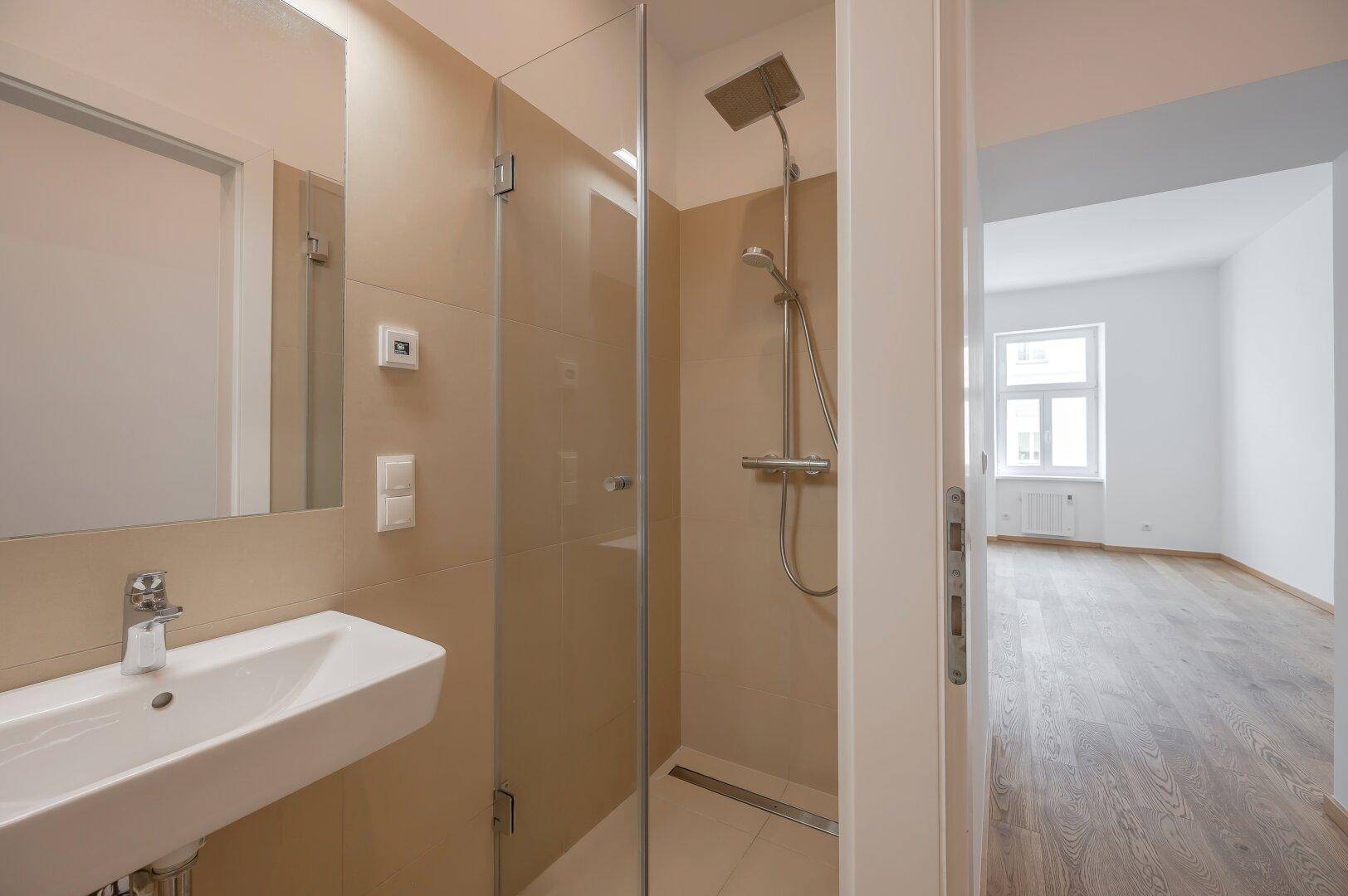 Modernes Badezimmer mit begehbarer Dusche, Waschbecken und Spiegel, in hellen Beigetönen gehalten.