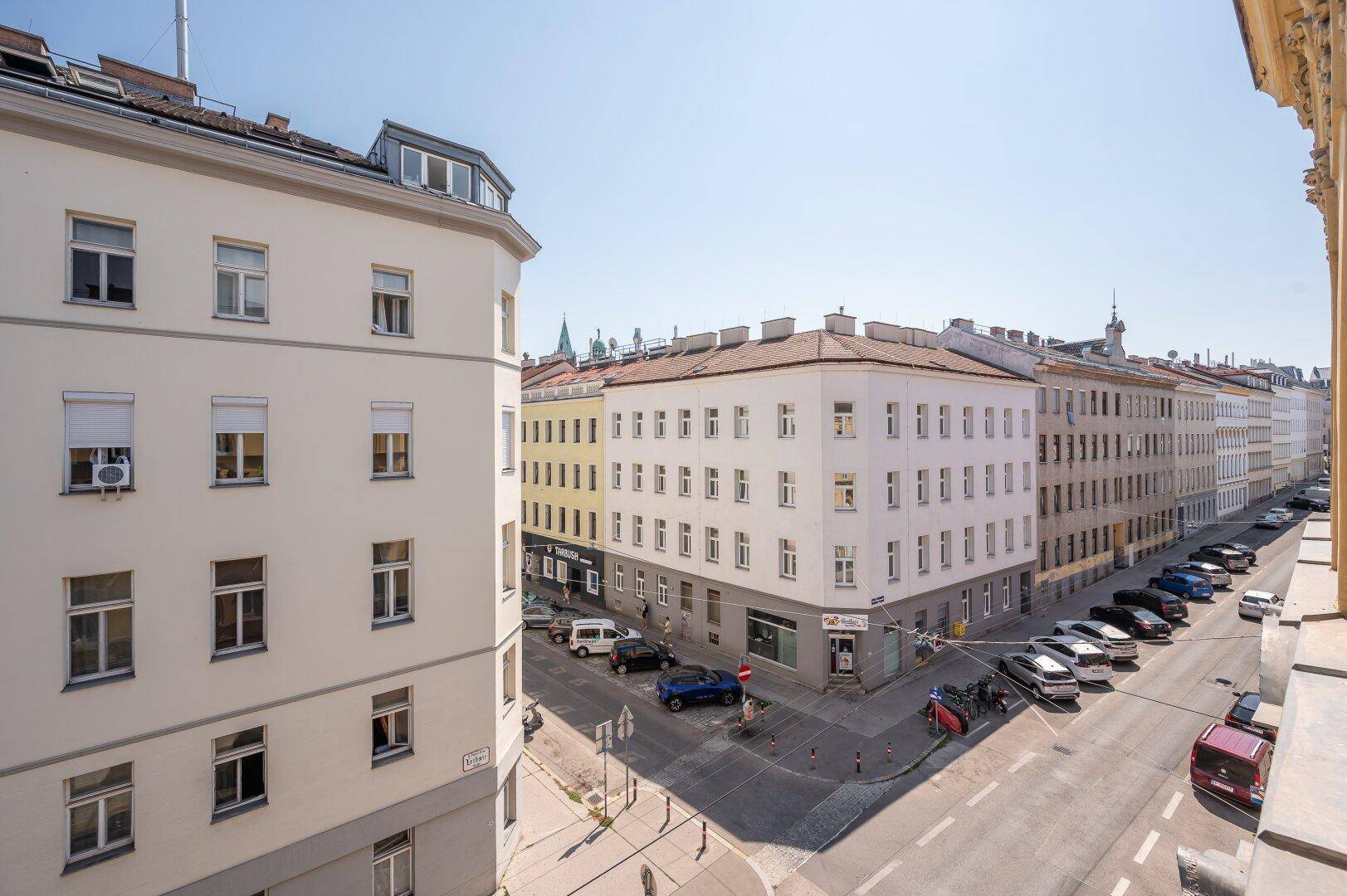 Blick von oben auf eine belebte Stadtstraße mit parkenden Autos und umliegenden Gebäuden.