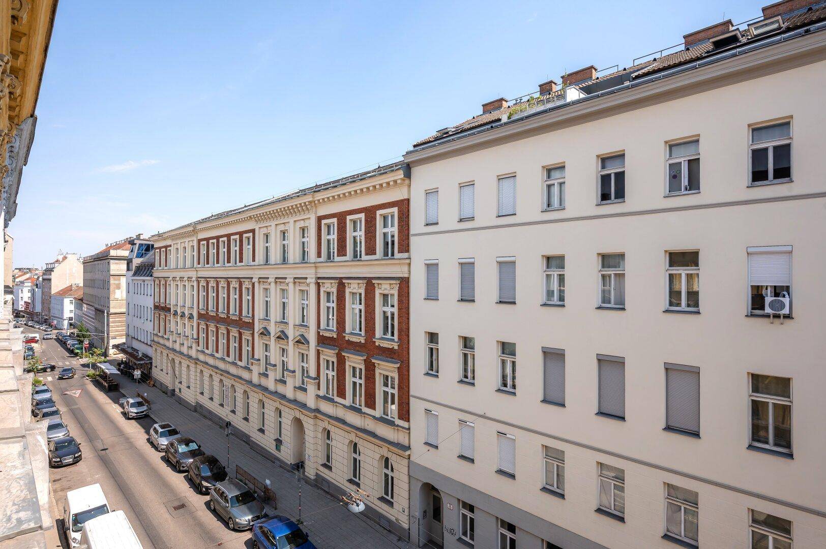 Weitläufiger Blick auf eine Stadtstraße mit historischen Gebäuden und parkenden Fahrzeugen.