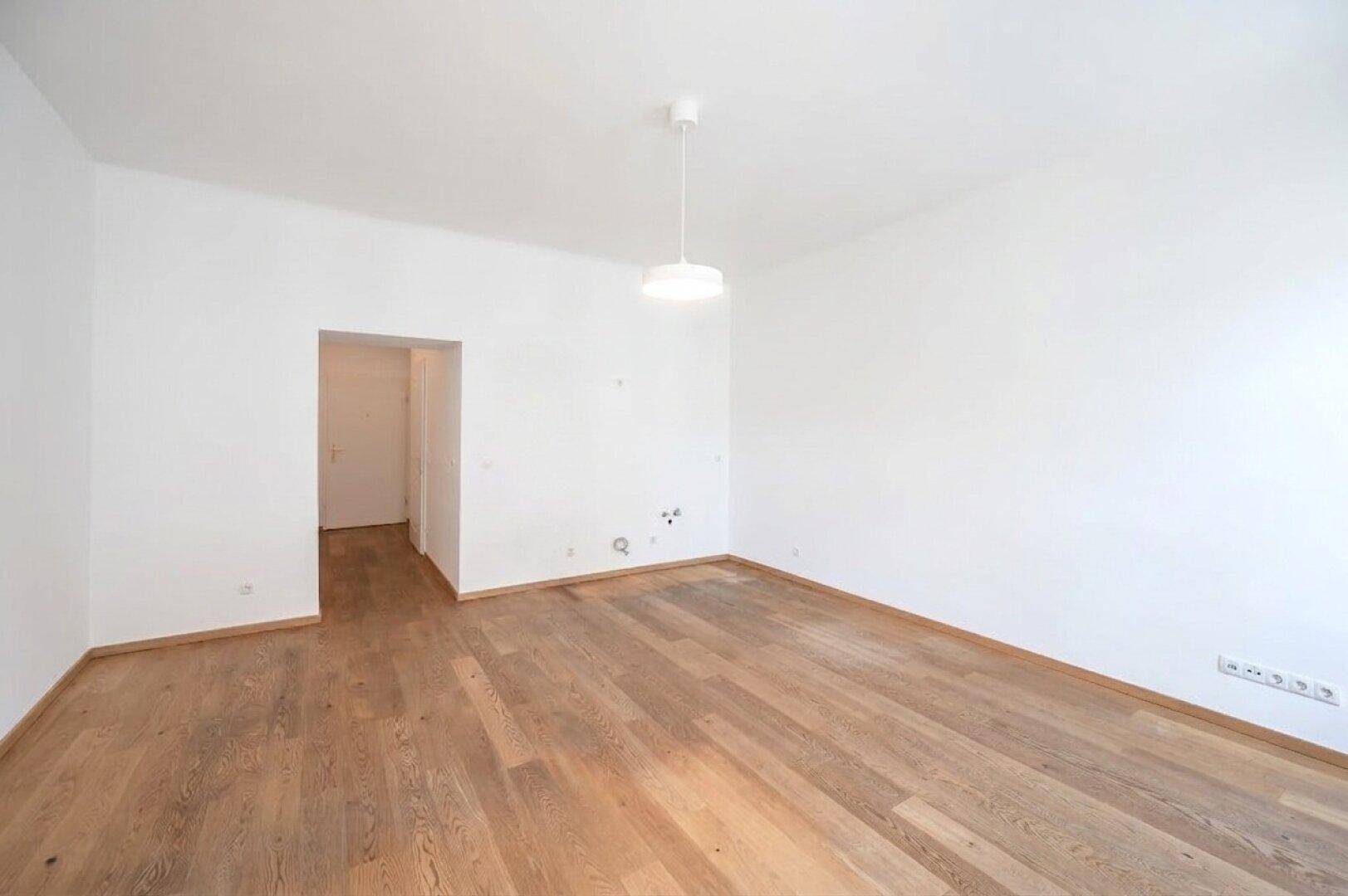 Geräumiger, leerer Raum mit hellem Holzboden und weißen Wänden, bereit zur individuellen Gestaltung.