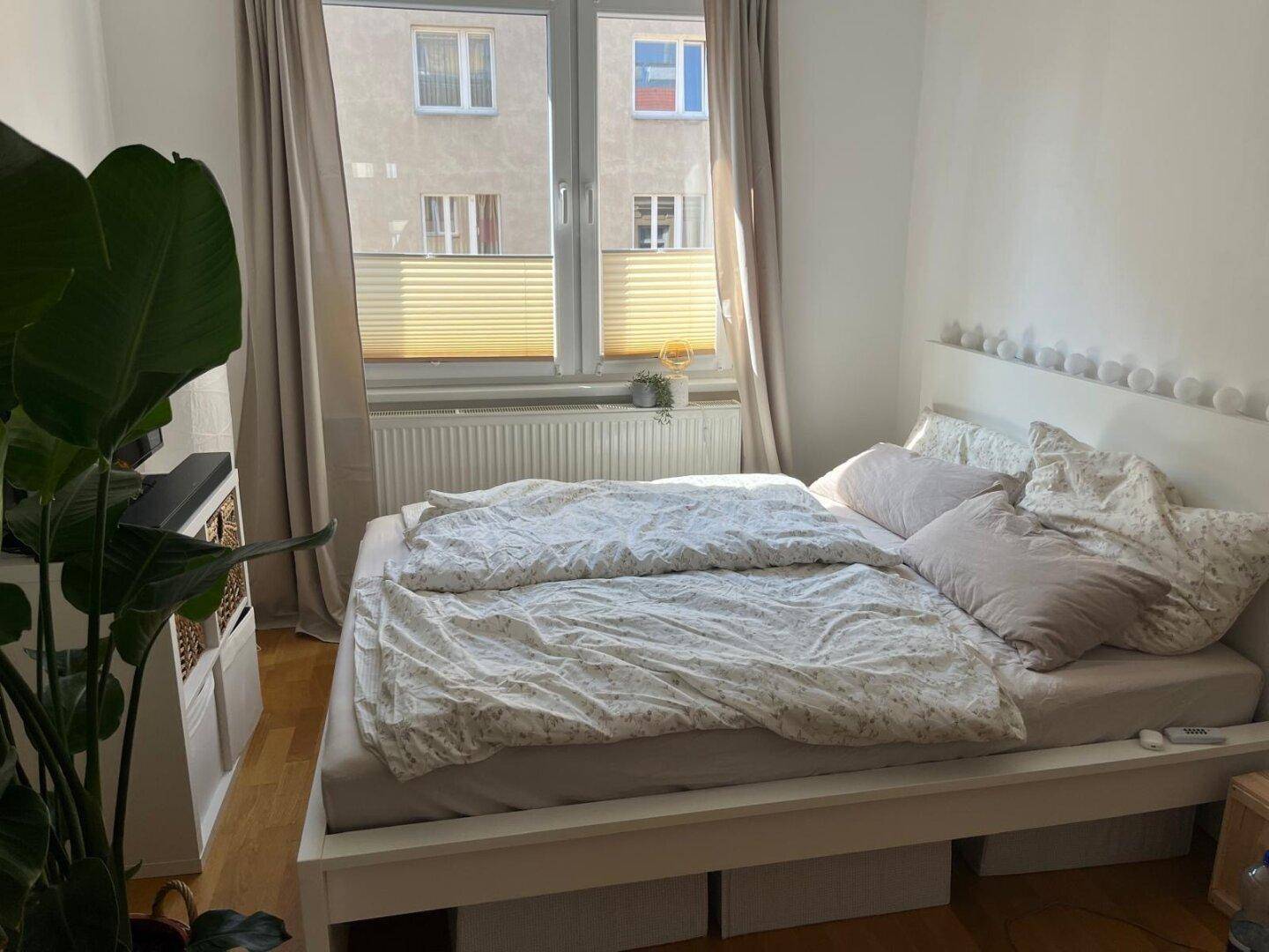 Helles Schlafzimmer mit großem Bett, Holzboden und Blick auf die umliegenden Gebäude.