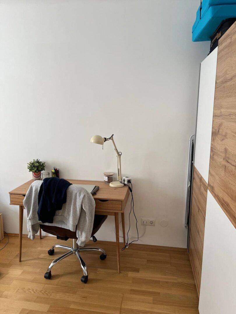 Kleiner Arbeitsbereich mit Holzschreibtisch, Bürostuhl und hellem Holzboden.
