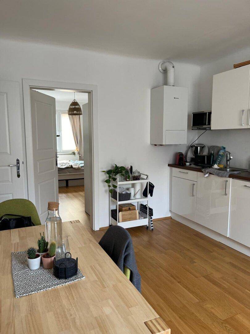 Offener Wohn- und Essbereich mit Holztisch und Blick in das angrenzende Schlafzimmer.