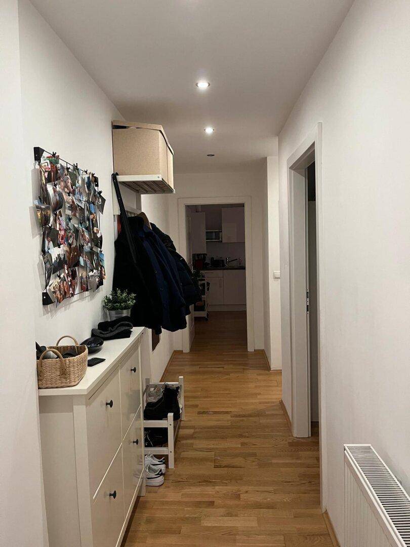 Langer Flur mit Holzboden, Garderobe und Schuhschrank, der zur Küche führt.