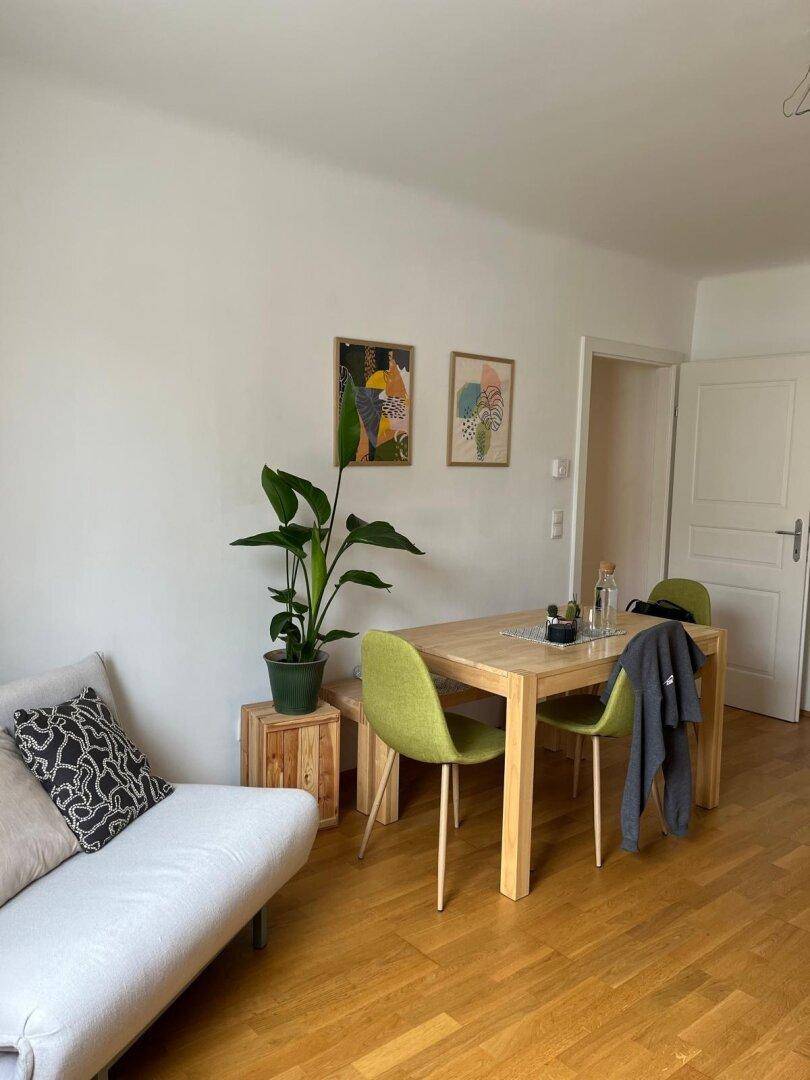 Heller Wohnbereich mit Sofa, Esstisch und modernen Bildern an der Wand.