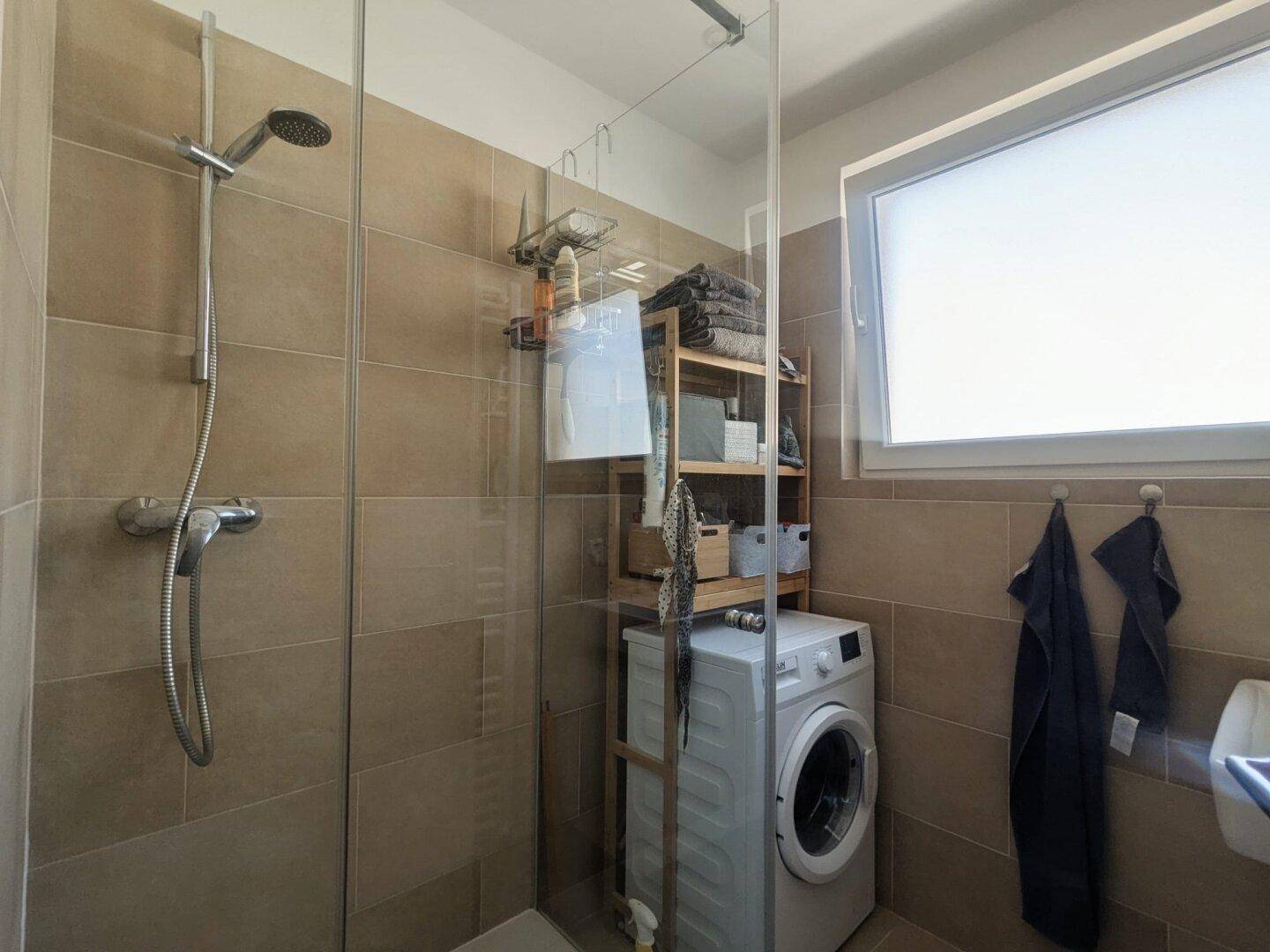 Modernes Badezimmer mit Dusche, Waschmaschine und Fenster für Tageslicht.