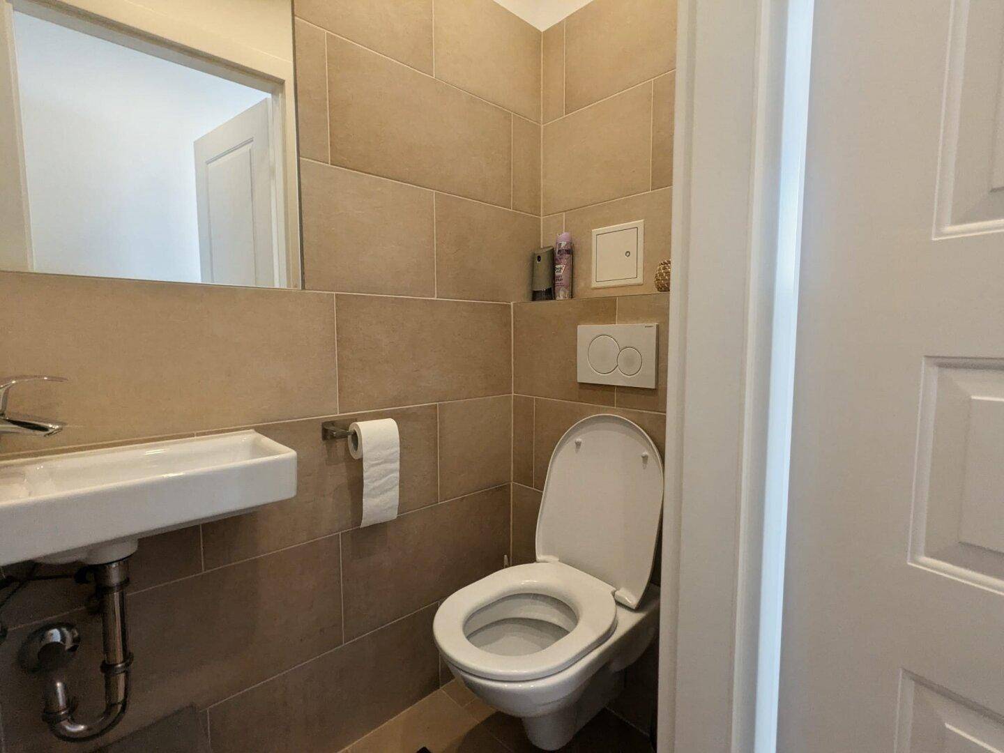 Modernes Gäste-WC mit beigen Fliesen, wandhängendem WC und kleinem Waschbecken.