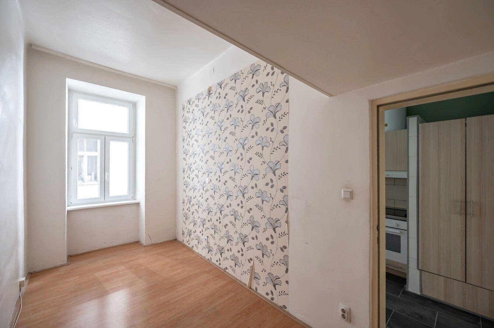 Helles Zimmer mit floraler Tapete an einer Wand und Holzboden, ideal für eine Neugestaltung.