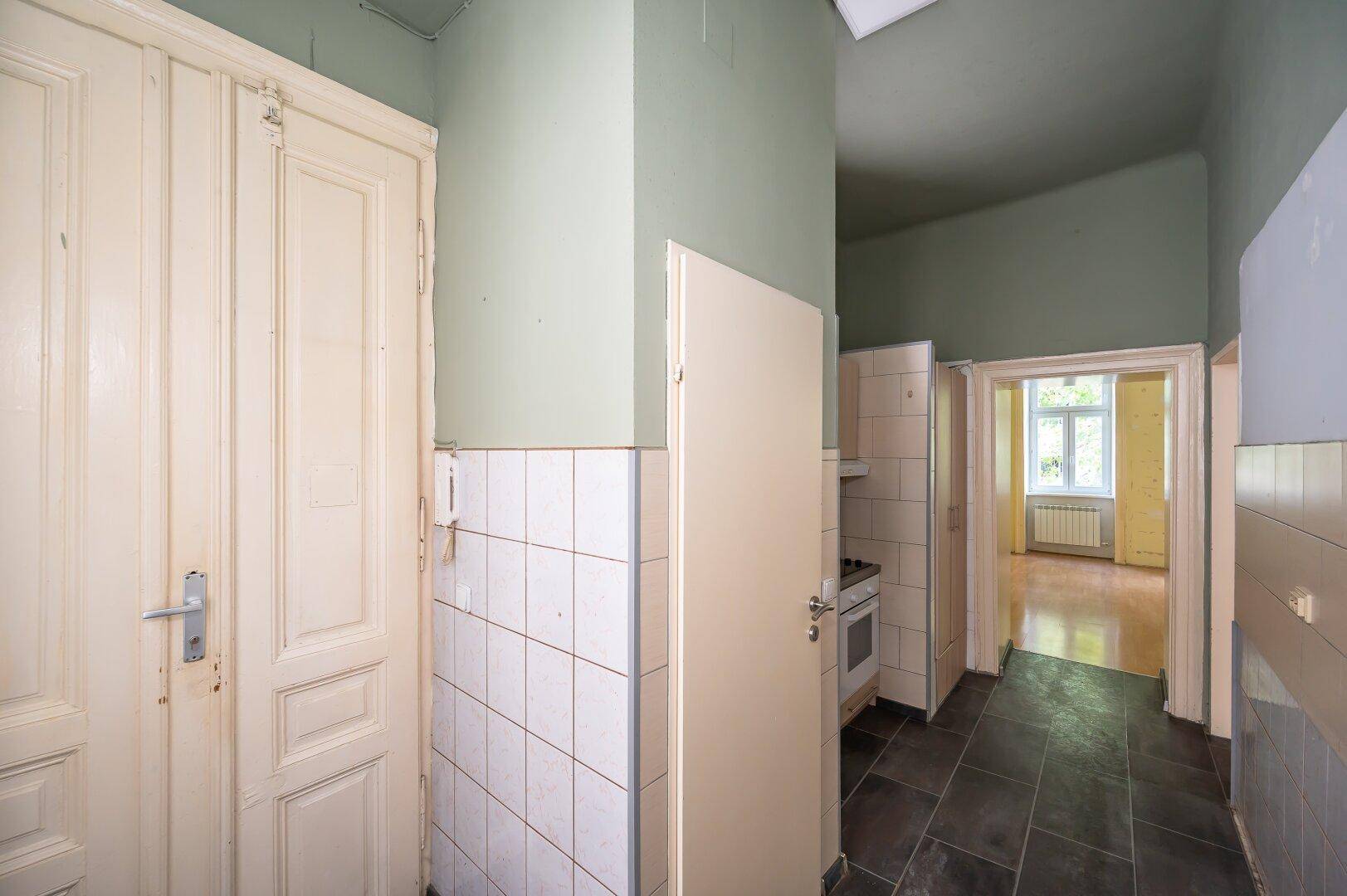 Langer Flur mit Fliesenboden und alten Holztüren, führt in den Küchenbereich.