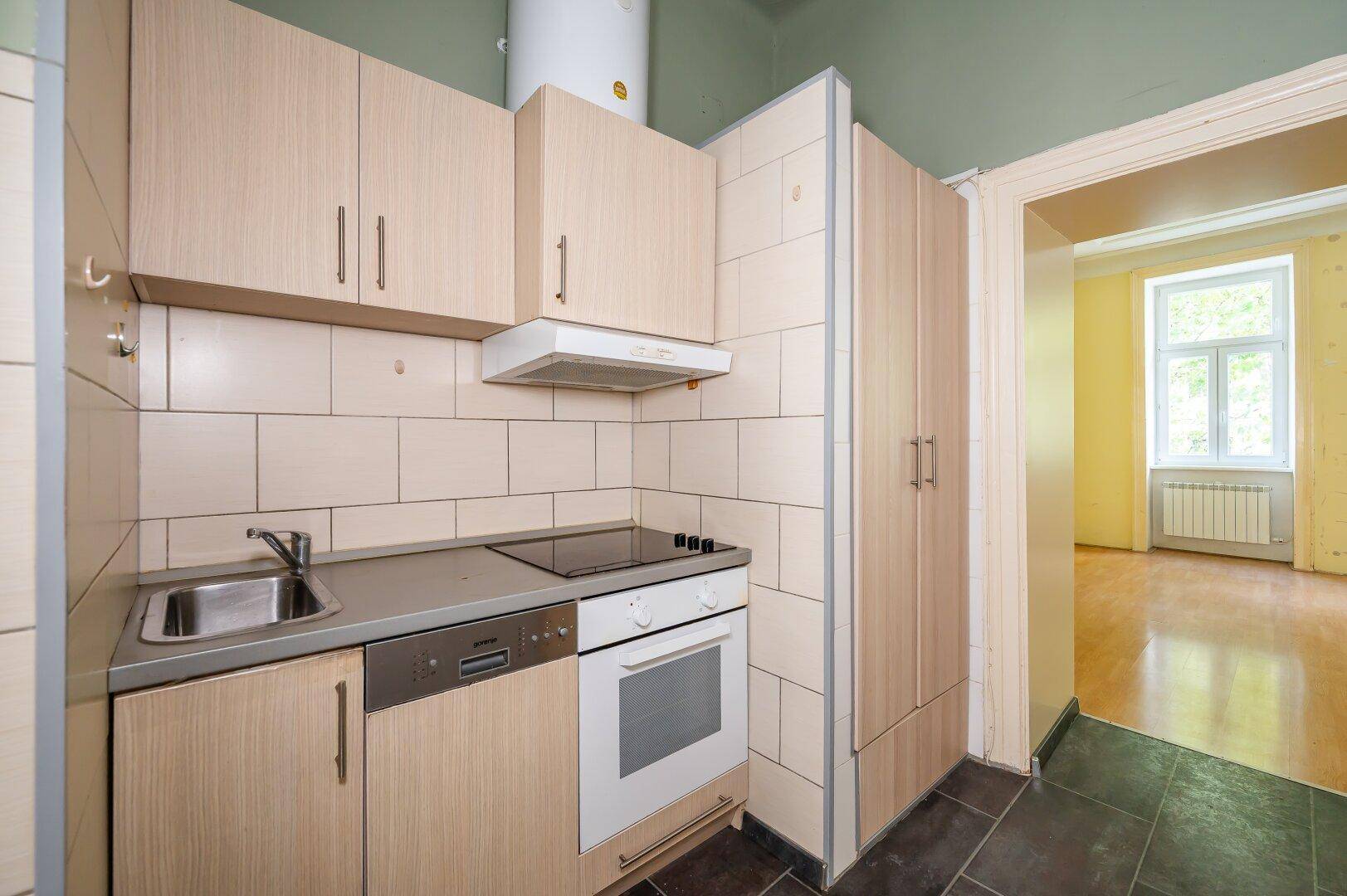 Kleine Einbauküche mit Holzschränken, Spüle, Herd und Geschirrspüler, funktional ausgestattet.
